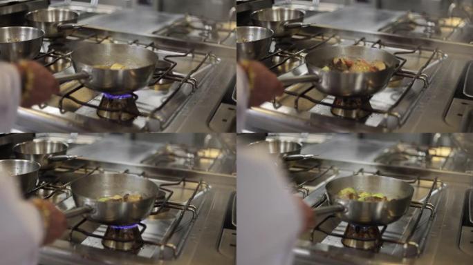 厨师手工在煎锅中烹饪食物的特写镜头在煤气炉上，专业厨师在晚餐的商业厨房中烹饪时在平底锅中搅拌肉，烹饪