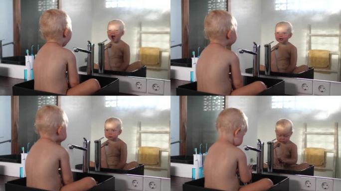 一个可爱的金发碧眼的白人小孩坐在一个方形的黑色设计师水槽里，一边看着镜子里的自己，一边用水玩儿童游戏