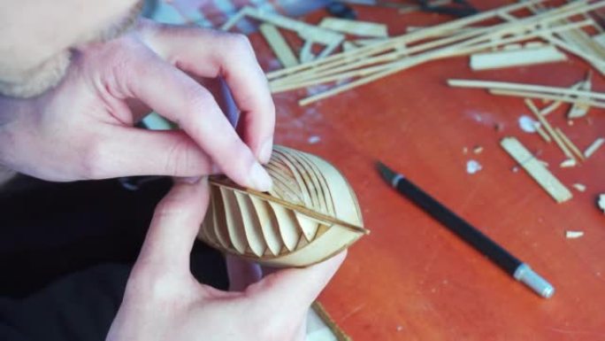 人的手用胶水粘合船模胶合板细节，用手指握住。建造玩具船的过程，爱好，手工艺。工作台有各种材料、零件和