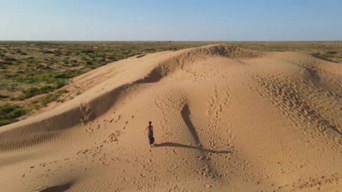 无人机的鸟瞰图。夏天，在阿斯特拉罕 (Astrakhan)，穿着长豹子连衣裙的女人沿着沙漠中的高沙丘