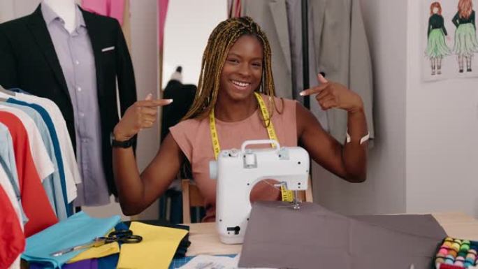 非裔美国女性裁缝微笑着自信地指着自己在裁缝店