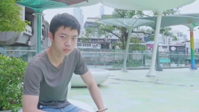 一个年轻的亚洲男孩，高个子，聪明，英俊，穿着t恤，牛仔裤，站着玩他的智能手机