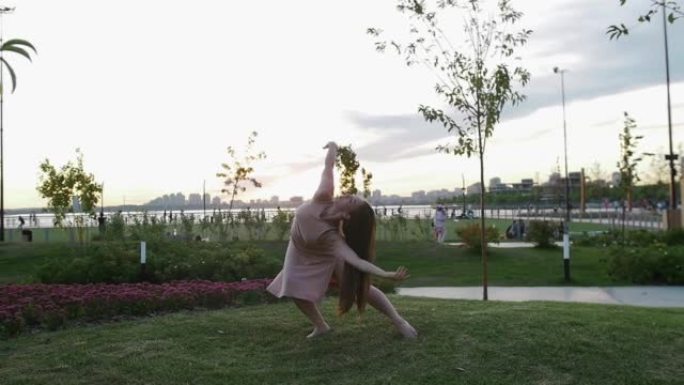 穿着米色连衣裙的女人在公园的草地上跳舞，赤脚慢动作