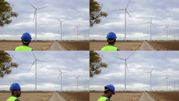 男性可再生能源工程师，带建筑头盔和反光背心，检查风电场中的风塔