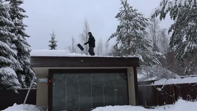 在冬季霜冻的日子里，男人用铁锹从房屋屋顶，公寓楼打扫雪。