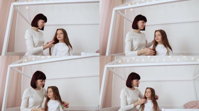 开朗的年轻高加索母亲坐在木床上梳理女儿的头发
