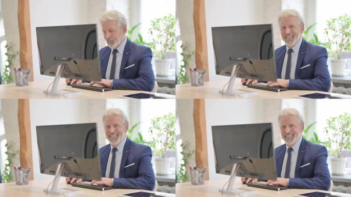 资深老商人在使用台式电脑时对着镜头微笑