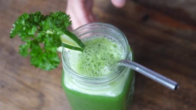 借助冷榨果汁清洁体内毒素。一罐绿色果汁的俯视图，带有一枝欧芹和一根稳定的金属吸管。排毒概念。