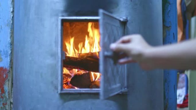 手打开壁炉门，家里的燃木炉被加热。原木躺在燃木火炉，红色火焰，舒适的家中。4k，普洛雷斯