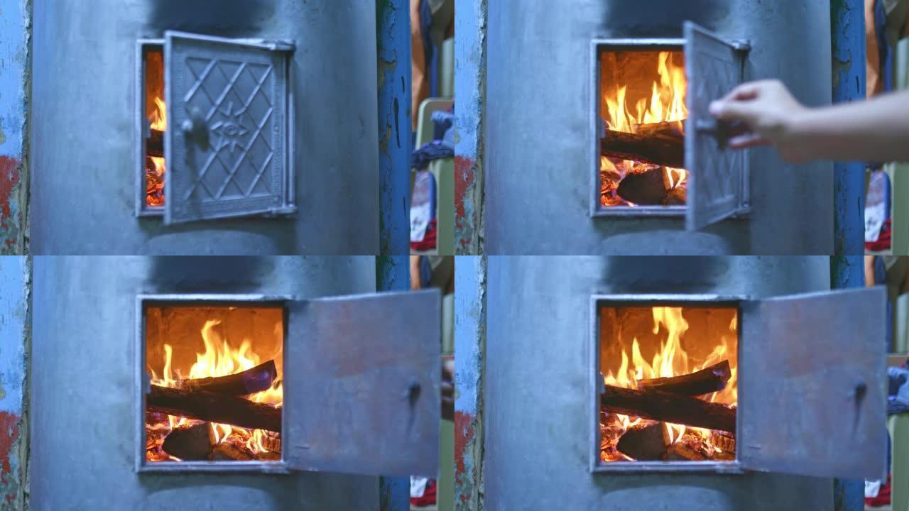 手打开壁炉门，家里的燃木炉被加热。原木躺在燃木火炉，红色火焰，舒适的家中。4k，普洛雷斯