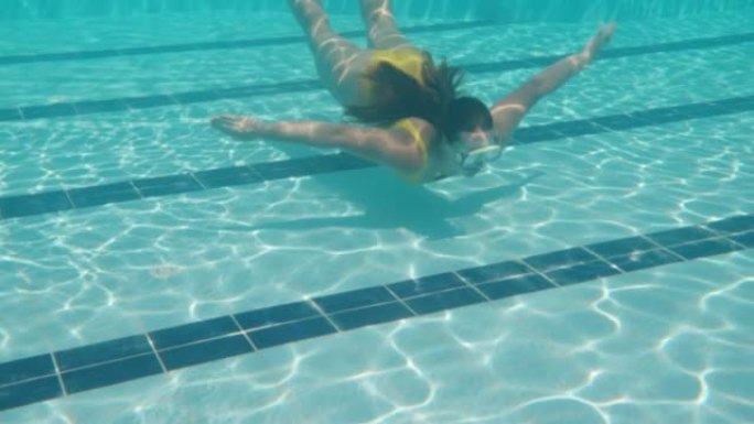 镜头在下面，有一个穿着黄色泳衣和面具的女孩。游泳池和水下相机。慢动作