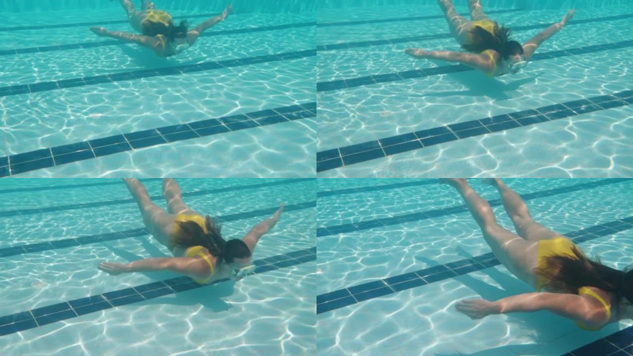 镜头在下面，有一个穿着黄色泳衣和面具的女孩。游泳池和水下相机。慢动作
