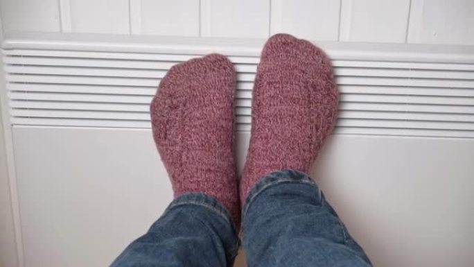 针织袜子中的腿在电加热器上变暖。冻人穿着温暖的羊毛袜子冻着冬天的寒冷。呆在家里不舒服。人们在现代散热