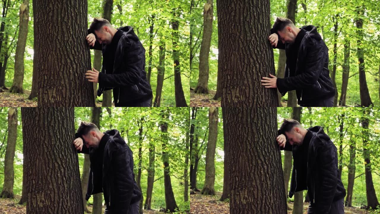 沮丧的男性脸悲伤的压力男人站在树林里的户外抱着头，因为深深的沮丧而哭泣，冒犯了面部表情担心麻烦问题。