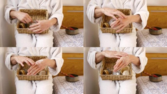浴袍中的女人在洗完澡后用有机护手霜为她的双手涂上奶油，这是自我护理的仪式。