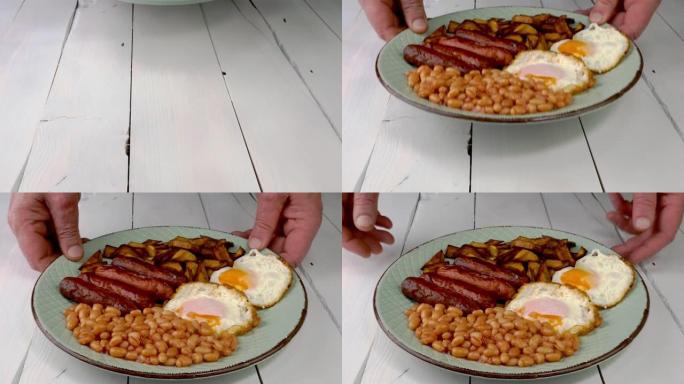人的手把英式早餐和煎蛋、香肠、豆子、土豆放在木桌上。