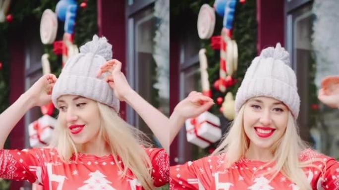 穿着红色新年礼服和针织冬帽的美丽金发女郎。跳舞，玩得开心。圣诞节和新年概念。垂直视频