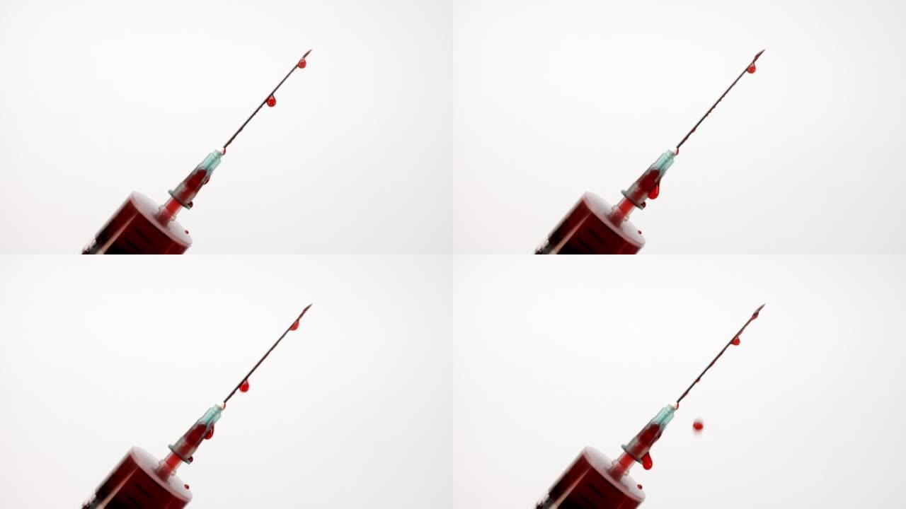 从注射器针头漏出的血滴。红色液体从白色背景上的注射器滴落