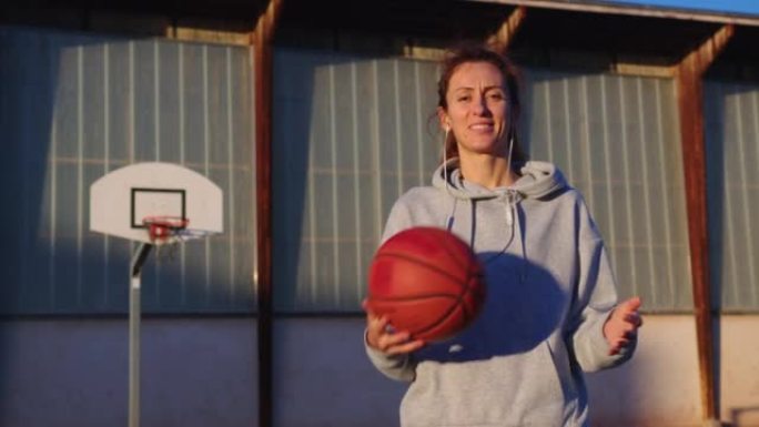 女子运动概念。一个穿着运动服的年轻快乐女人在篮球场上玩游戏。手中的橙色篮球