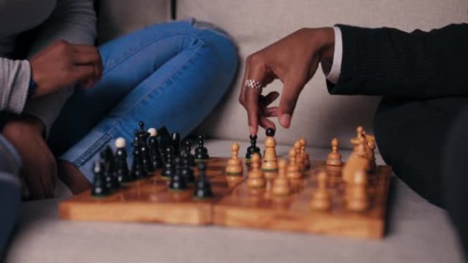 两个看起来像非洲的朋友下棋的手的特写。他们坐在沙发上，轮流行动。这个男孩的手指上有银色戒指。迷人的女
