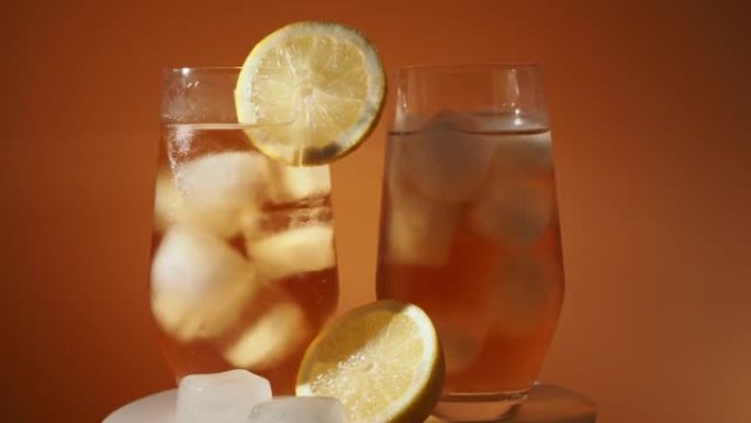 旋转冰茶在杯子里，橙色背景上有冰块。冰茶。