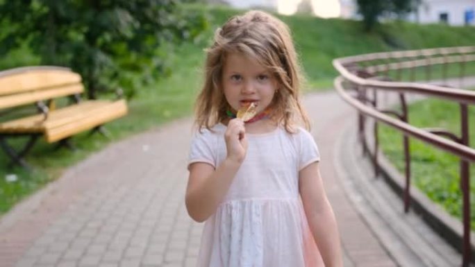 一个小女孩走在街上，用棍子特写吃糖。一个有糖果的孩子。快乐的孩子