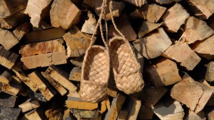 古董手工乡村鞋-韧皮鞋。柳条桦木树皮韧皮鞋挂在木柴的背景上。