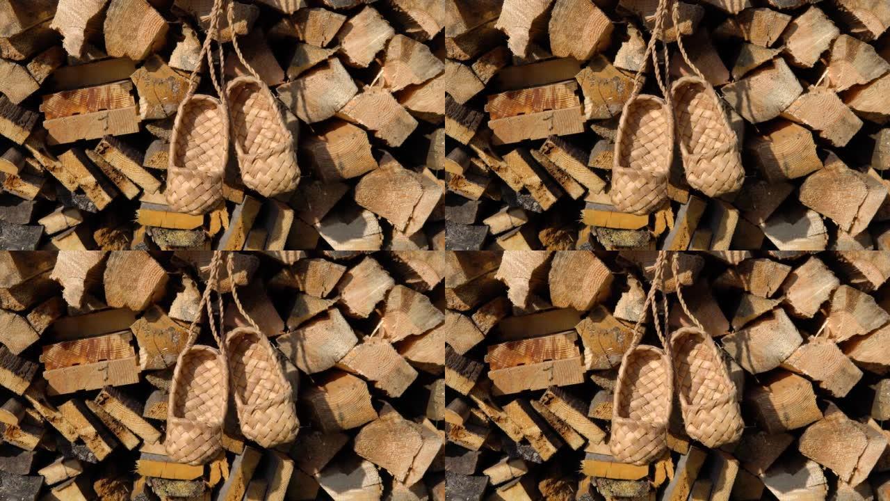 古董手工乡村鞋-韧皮鞋。柳条桦木树皮韧皮鞋挂在木柴的背景上。