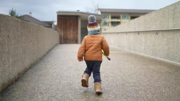 小男孩穿着冬装在城市公园走廊跑步。孩子戴着无檐小便帽和夹克。蹒跚学步的男孩赛跑者