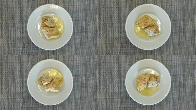 俯视图，白色鱼片配酱汁作为午餐菜。盘子旋转。美味健康的食物概念。
