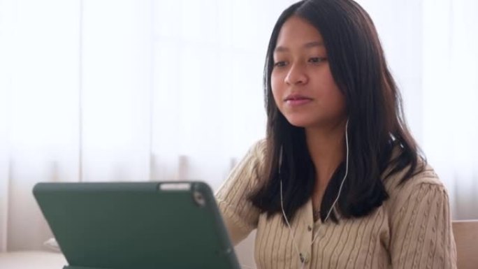亚洲女孩向在家使用数字平板电脑在线学习的老师问好