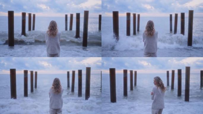孤独的年轻女子，长长的卷发，在汹涌的大海附近看着海浪