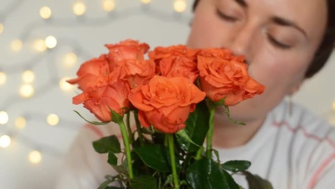 短发的年轻幸福的女人坐着一束红玫瑰。女孩轻轻地触摸花朵，闻到它们的香味。生日快乐。妇女节快乐。