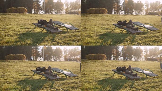 男人躺在秋天阳光明媚的公园的日光躺椅上，戴上兜帽。