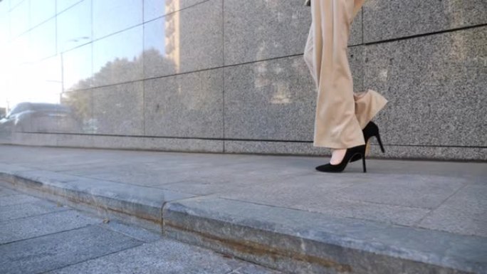 走在现代建筑附近的女商人的脚。穿着高跟鞋的女商人的腿在城市街道上。穿正装的成功女士通勤上班。职业概念