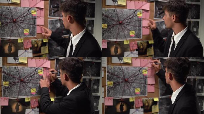 侦探看着木板，上面有指纹，照片，地图和线索，用红色的绳子在墙上连接，在办公室工作