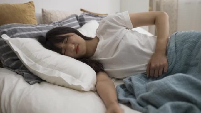 下腹部严重抽筋的亚洲女孩白天在家里的卧室里摸着肚子，躺在床上，脸上带着痛苦的表情。