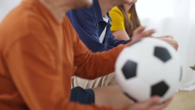 一群亚洲男女朋友一起在家里看电视上的足球运动。
