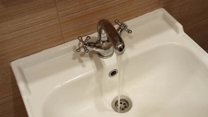 细水流从镀铬水龙头流入浴室的陶瓷水槽。特写，侧视图。