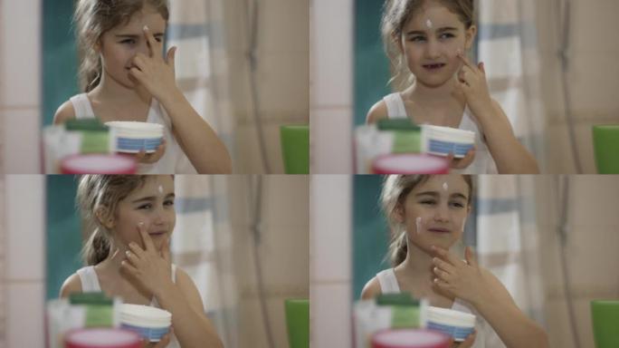 肖像年轻有趣的小女孩在浴室的脸上涂保湿霜，看着镜子反射。快乐可爱的高加索无牙儿童涂在皮肤汽车面霜上。