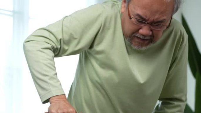 微笑着快乐的亚洲老年老人坐在沙发上，带着步行者或手杖在家，带着快乐和健康的生活方式。
