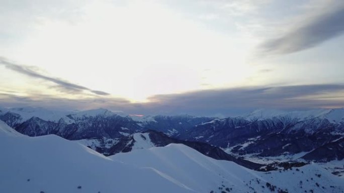 冬季日出时，雪山山坡上满是粉末的空中飞车在滑雪胜地进行自由滑行。偏远地区的山脉覆盖着初雪。高加索山峰