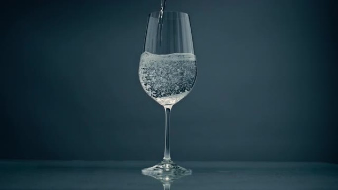 鼓泡水倒入玻璃在灰色背景特写。水晶透明液体