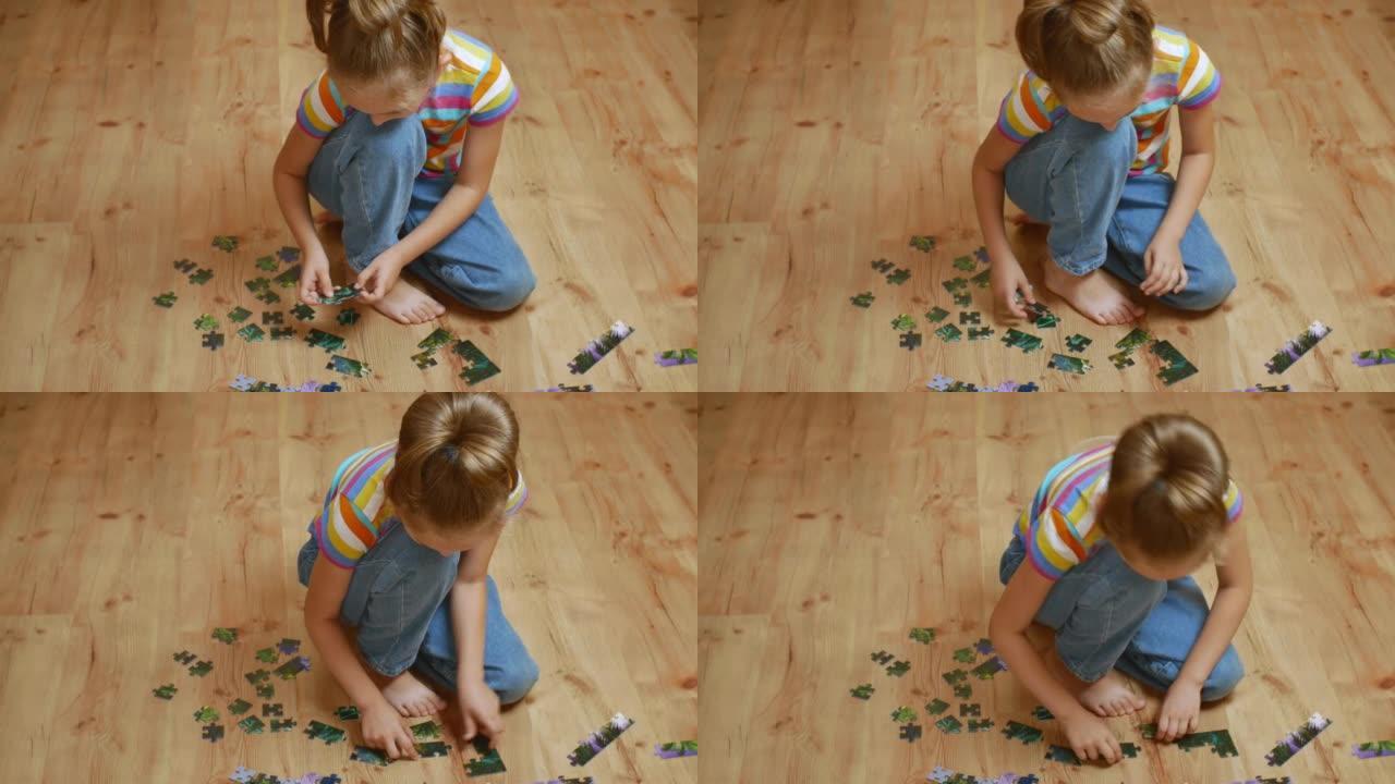 木地板上的一个小女孩热情地收集拼图。一个漂亮的女孩穿着灰色套头衫和蓝色牛仔裤，有兴趣在木地板上收集拼