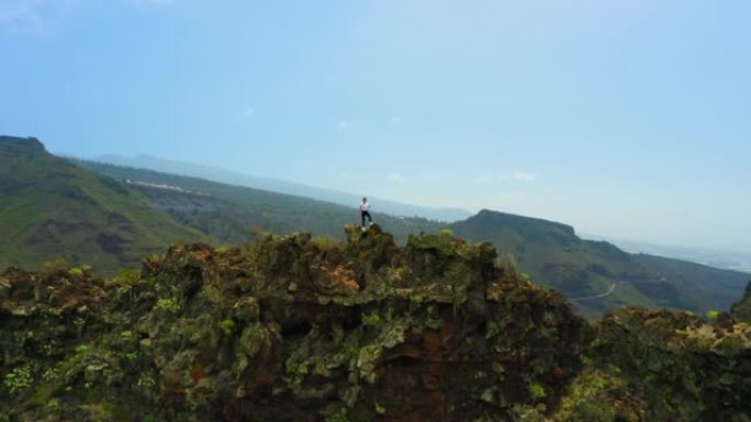 特内里费加那利岛。女人爬上了山顶。陡峭的岩石斜坡，沟壑。女孩徒步旅行者独自在火山山崖边享受。沉思绿色