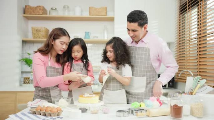 亚洲迷人的夫妇和女儿在家里的厨房里做蛋糕。幸福的家庭 -- 父亲、母亲和年轻女孩玩得开心，一起使用配