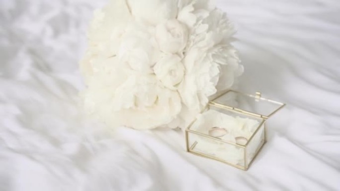 玻璃盒中的订婚戒指和白色亚麻上的白色花束的特写镜头