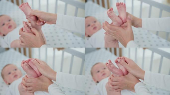 女人的特写镜头握着婴儿的腿，用手轻轻地抚摸着他的小脚，皮肤完美。婴儿护理概念