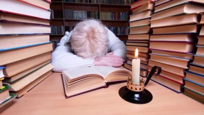 悲伤的女人在图书馆使用蜡烛阅读书。能源危机概念。缺乏暖气和电力照明。