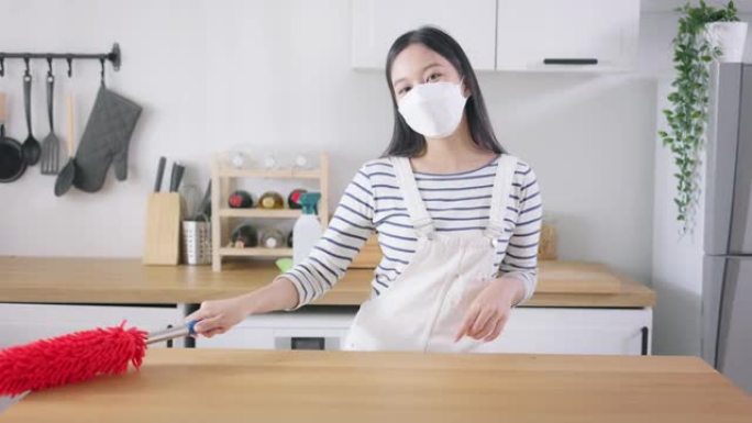 年轻快乐的亚洲妇女打扫家，戴着口罩，玩得开心。漂亮的清洁服务工人家政和整理厨房。家务和家务概念